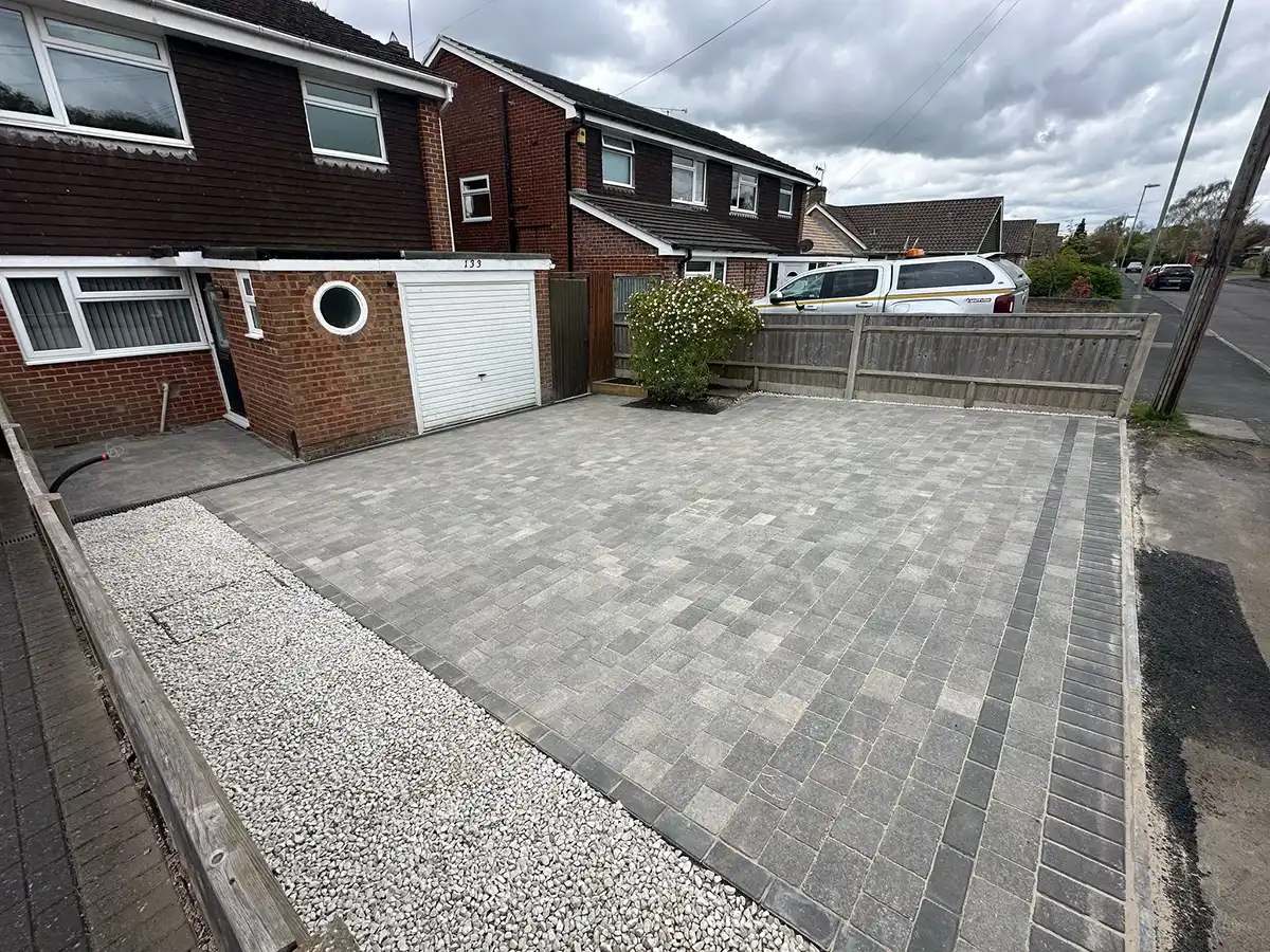 A paved driveway with a gravel border, adjacent to a house with a round window and a garage door, under a cloudy sky.